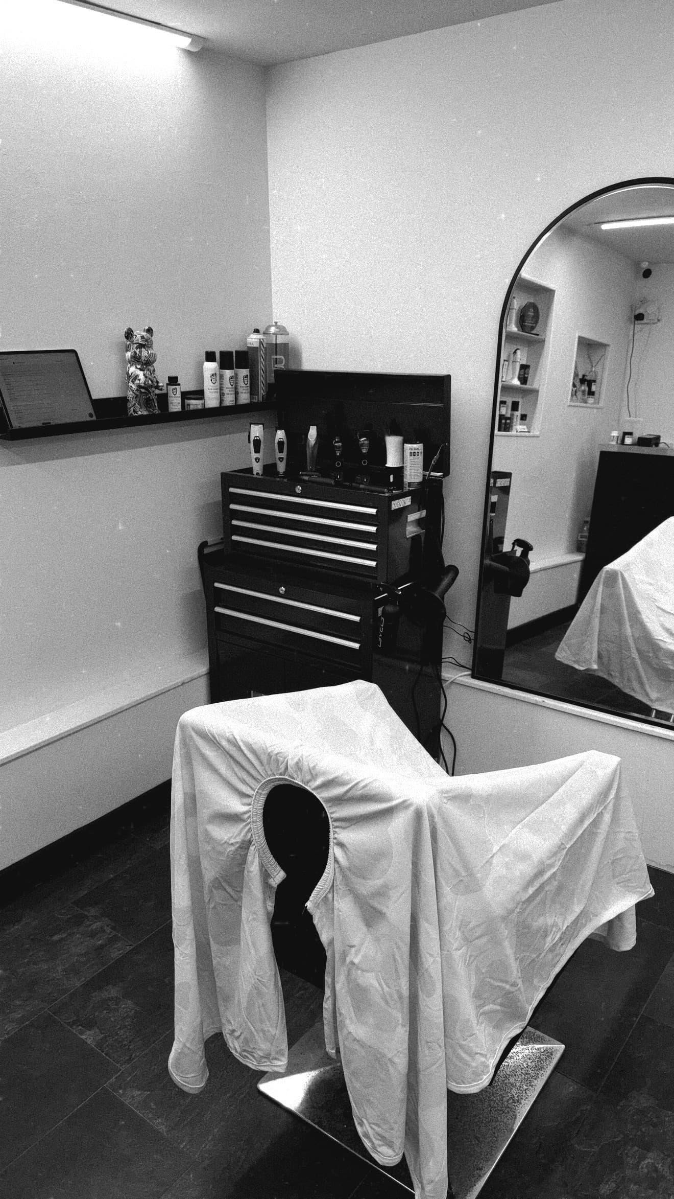 Draped barber chair, tool chest, and arched mirror in a black and white barbershop.